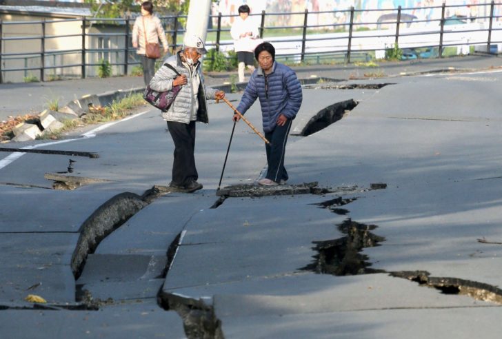 Local residents look at cracks caused by an earthquake on a road in Mashiki town