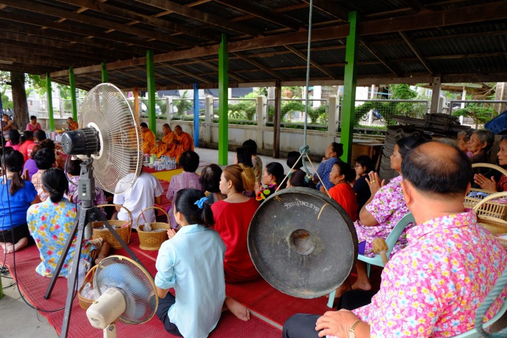 ชาวบ้านฟังพระสวดมนต์ แล้วฉันเช้า โดยมีผู้ใหญ่บ้านตีฆ้องสัญญาณ