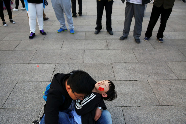 A man holds a sleeping child as people gather in Tiananmen Square to celebrate National Day in Beijing