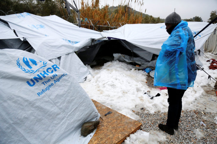 A migrant is covered with a plastic cover to protect from low temperatures as snow lays next to tents provided by the UNHCR at the refugee camp of Moria on the Greek island of Lesbos