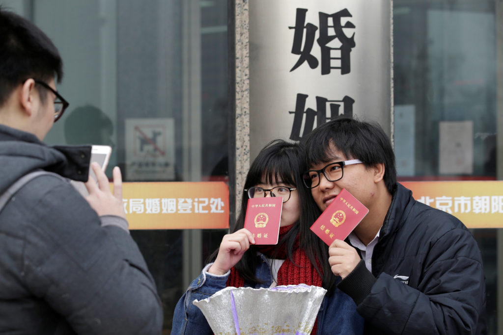 A new couple holding marriage certificates poses for a photo outside a registry office of marriage on Valentine's Day in Beijing, China, February 14, 2017. REUTERS/Jason Lee