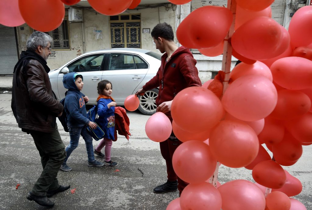 A Syrian man hands a balloon to a girl in front of a shop selling Valentine's day gifts in the northeastern city of Qamishli on February 13, 2017. / AFP PHOTO / DELIL SOULEIMAN