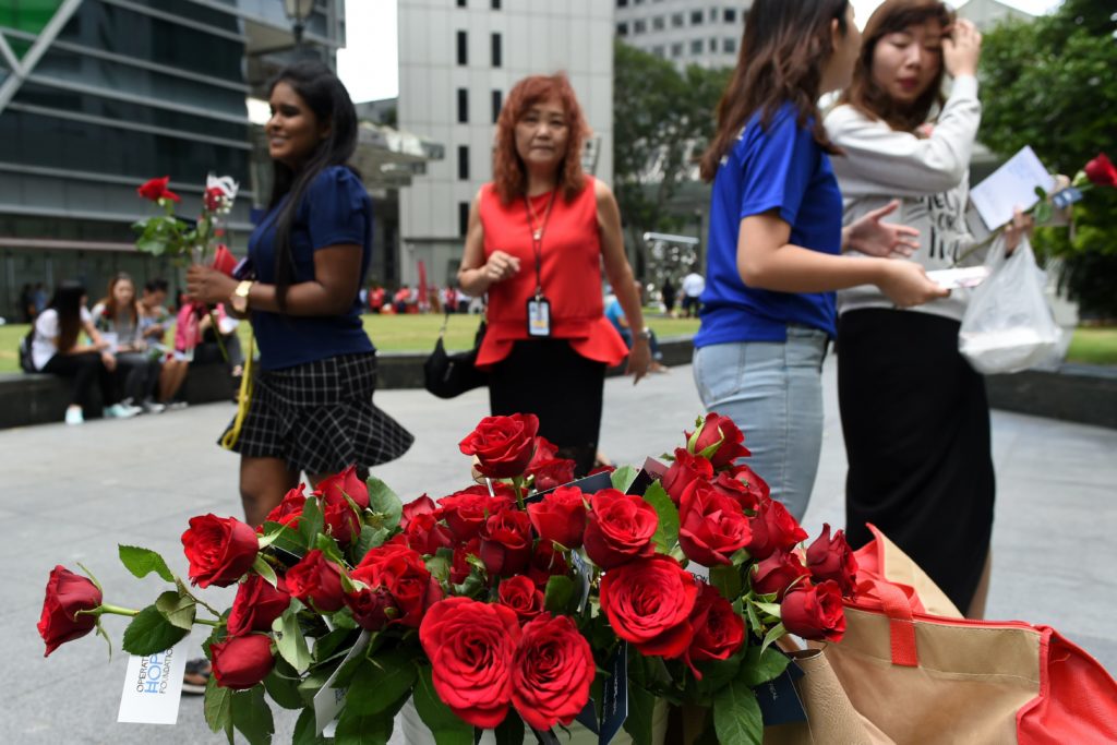 A member of the Operation Hope foundation (2nd R) distributes roses to passersby during Valentine's Day at Raffles Place business district in Singapore on February 14, 2017. / AFP PHOTO / Roslan RAHMAN