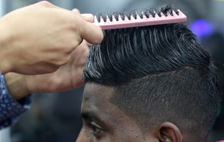 Palestinian barber Ramadan Odwan combs the hair of a customer after straightening and styling it with fire at his salon in Rafah, in the southern Gaza Strip