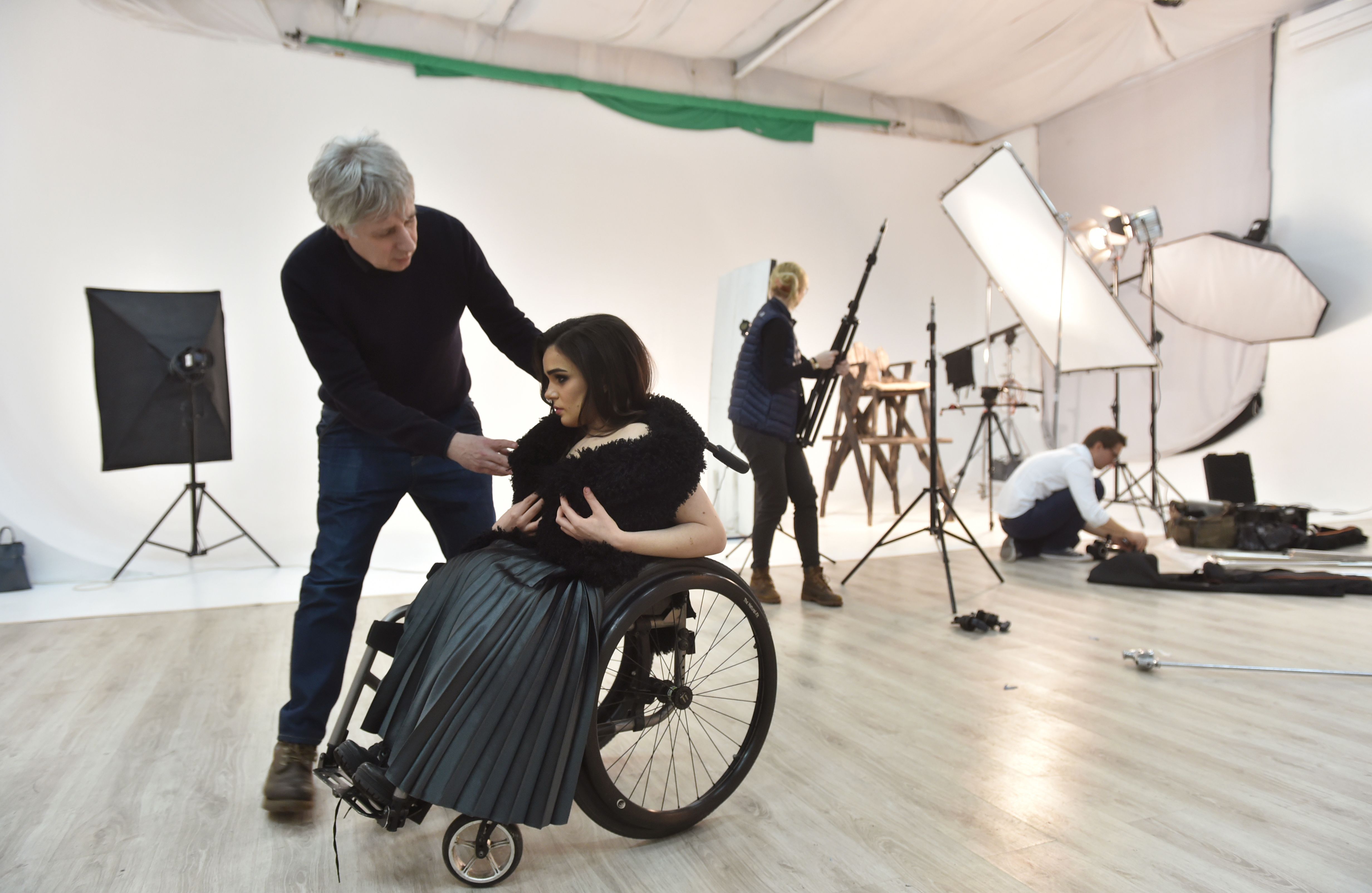 TO GO WITH AFP STORY BY OLGA SHYLENKO Ukrainian fashion designer Fedir Vozianovmakes (L) makes adjustments to a creation worn by Ukrainian model Alexandra Kutas, who is in a wheelchair since birth due to cerebral palsy,  prior to a photo and video fashion shoot in Kiev on January 25, 2017. Kutas, 23, is Ukraine's first model with a disability to headline a runway event of this level, after covering a long and thorny path for her dream to come true. / AFP PHOTO / Sergei SUPINSKY