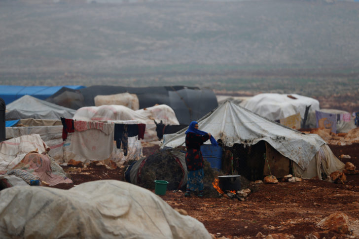 A displaced Syrian woman stands outside of her tent at Kelbit refugee camp in Idlib province