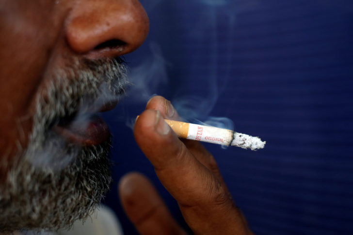 A man holds a Capstan cigarette, which is the brand of Pakistan Tobacco Company, as he exhales smoke in Karachi