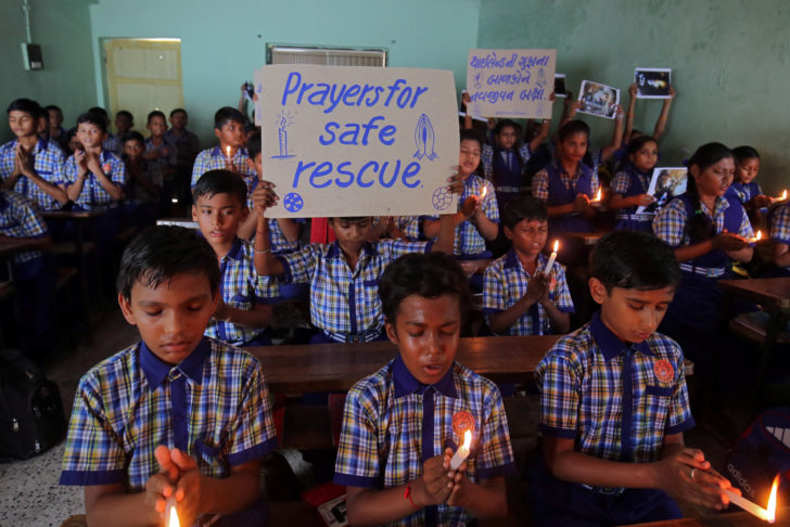 Schoolchildren pray for the schoolboys who are trapped inside a flooded cave in Thailand's northern province of Chiang Rai, at a school in Ahmedabad