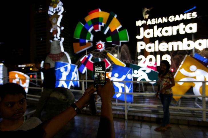 People take pictures next to an installation sign promoting the 18th Asian Games in central Jakarta