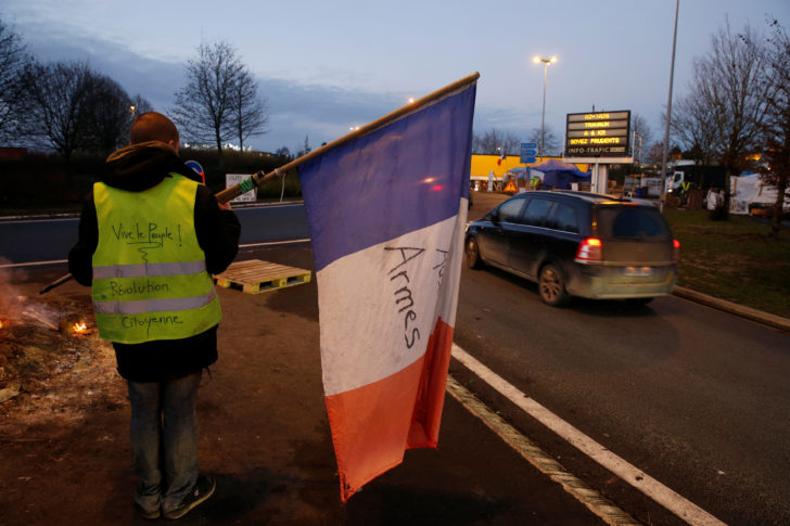 A protester wearing a yellow vest, the symbol of a French drivers' protest against higher fuel prices, holds a flag at the approach to the A2 Paris-Brussels Motorway, in Fontaine-Notre-Dame