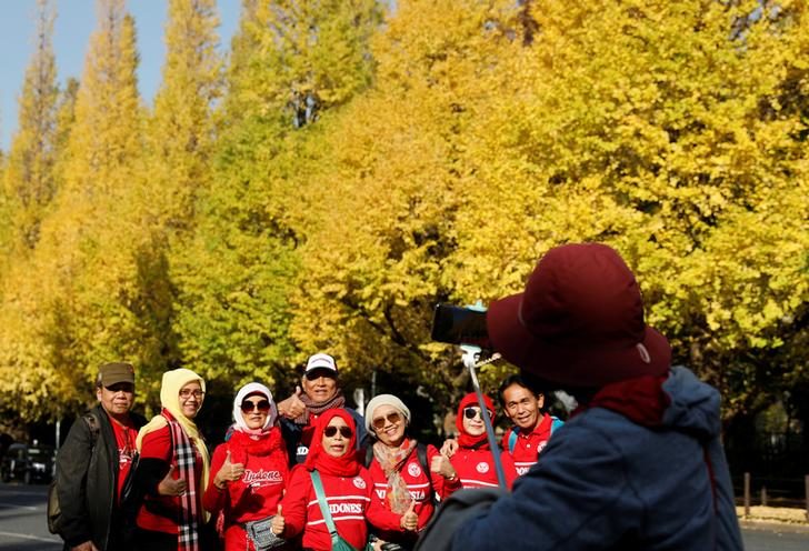 Tourists pose for a photo in front of yellow ginkgo trees in Tokyo