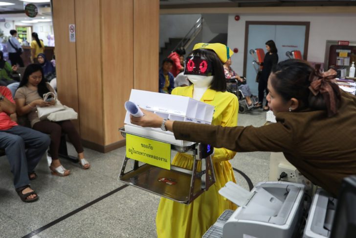 A hospital staffer receives medical documents from a robot wearing a nurse costume at Mongkutwattana General Hospital in Bangkok
