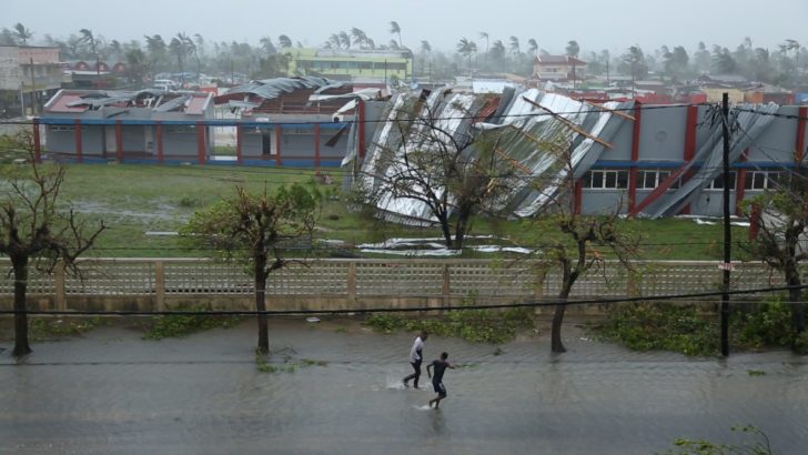 People walk down a flooded road next to buildings damaged by Cyclone Idai in Beira
