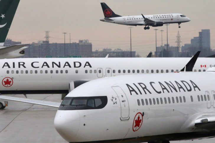 FILE PHOTO: Two Air Canada Boeing 737 MAX 8 aircrafts are seen on the ground as Air Canada Embraer aircraft flies in the background at Toronto Pearson International Airport