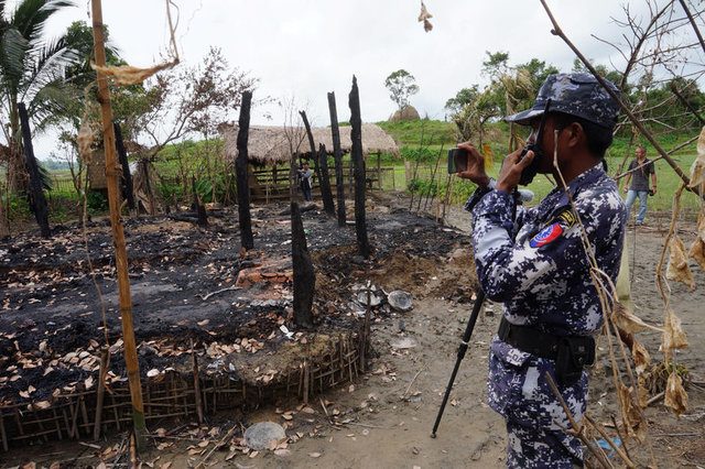 A Myanmar border guard police officer takes pictures at the remains of a burned house in Tin May village, northern Rakhine state, Myanmar