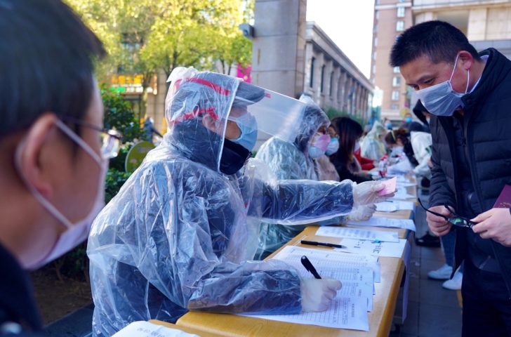 Community workers wearing makeshift protective suits help residents to register for coupons to purchase face masks at pharmacies, in Shanghai