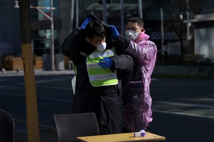 A security guard wearing a plastic raincoat helps his colleague to put on a hood at a checkpoint before an office building, in Beijing's tech hub Zhongguancun