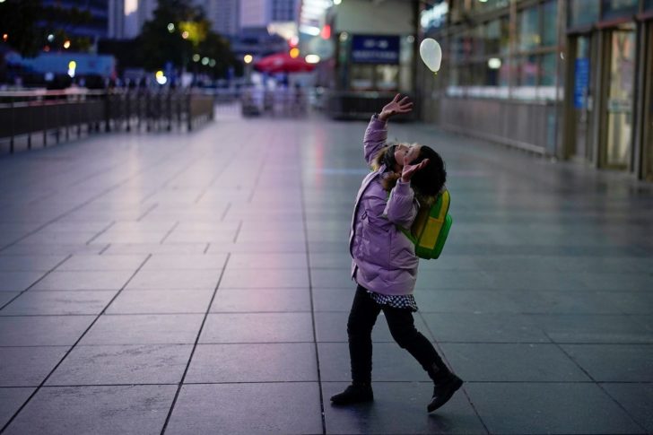 A girl wearing a face mask plays with a balloon near the Shanghai railway station as the country is hit by an outbreak of the novel coronavirus, in Shanghai