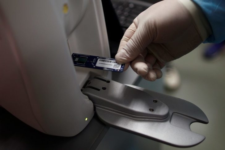 A Home Team Science & Technology Agency (HTX) scientist loads a Veredus Lab-on-Chip molecular testing chip used in their coronavirus test kits into an optical reader for reading the results off a microarray built into the chip, in Singapore