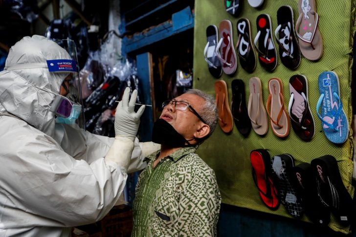 A healthcare worker in protective gear collects a swab sample to be tested for the coronavirus disease (COVID-19) from a vendor at a traditional market in Jakarta, Indonesia