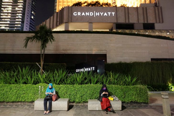 Women wearing protective masks sit outside the Grand Hyatt hotel, following the coronavirus disease (COVID-19) outbreak, in Jakarta