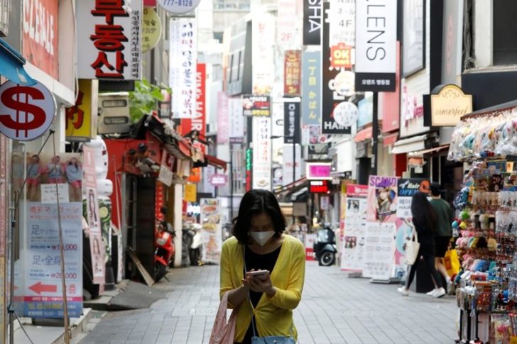 A woman wearing a mask looks at her mobile phone amid social distancing measures to avoid the spread of the coronavirus disease (COVID-19), in Myeongdong shopping district in Seoul