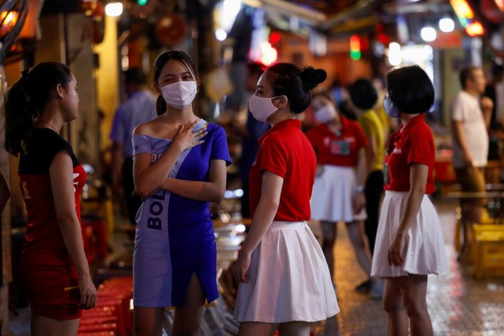 Beer brand promoters wearing protective masks are seen as they wait for customers in front of a bar, at Ta Hien night street in Hanoi