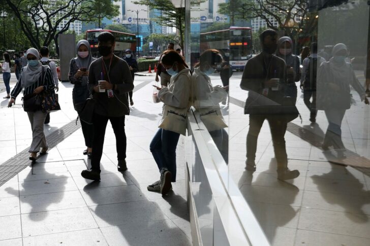 People wearing protective masks are reflected in a glass as they walk outside a shop, amid the coronavirus disease (COVID-19) outbreak in Kuala Lumpur