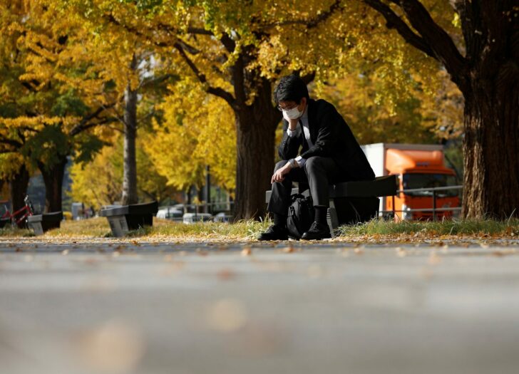 A man wearing a protective face mask pauses under colourful autumn leaves, amid the coronavirus disease (COVID-19) outbreak, in Tokyo