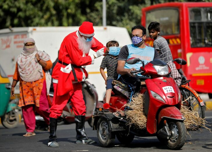 A man wearing a Santa Claus costume distributes free masks on an intersection in Ahmedabad