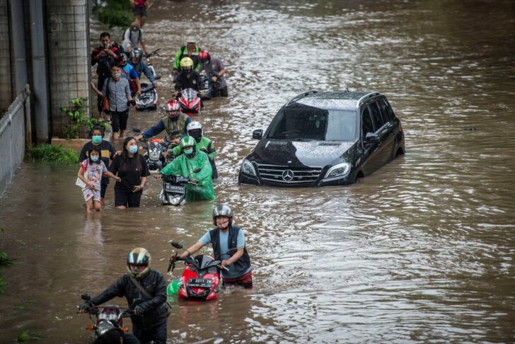 People push their motorbikes through water in an area affected by floods following heavy rains in Jakarta