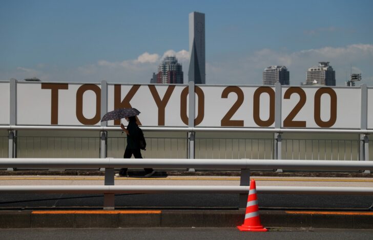 FILE PHOTO: A woman shelters from the sun under an umbrella as she walks past Olympics signage