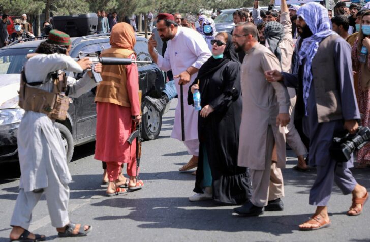 FILE PHOTO: A member of the Taliban forces points his gun at protesters, as Afghan demonstrators shout slogans during an anti-Pakistan protest, near the Pakistan embassy in Kabul, Afghanistan