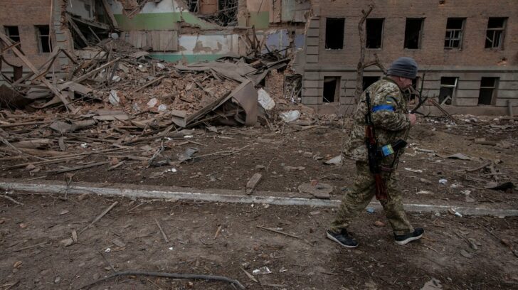 A Ukrainian service member walks past a destroyed building in the town of Okhtyrka
