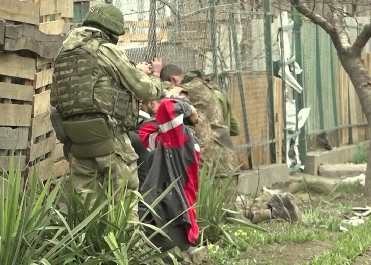 An armed serviceman stands near kneeling soldiers in a location given as Mariupol