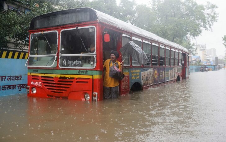 A man attempts to get off a bus after it broke down on a flooded street amidst heavy rainfall in Mumbai