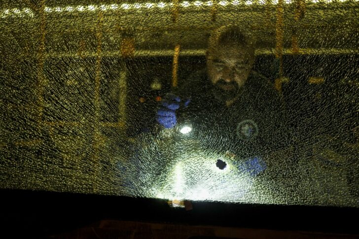 An Israeli security personal stands behind a shattered window of a bus as he checks it following an incident in Jerusalem