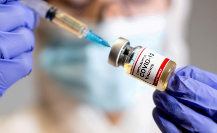 A woman holds a medical syringe and a small bottle labelled