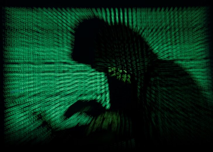 Hooded an holds laptop computer as cyber code is projected on him in this illustration picture