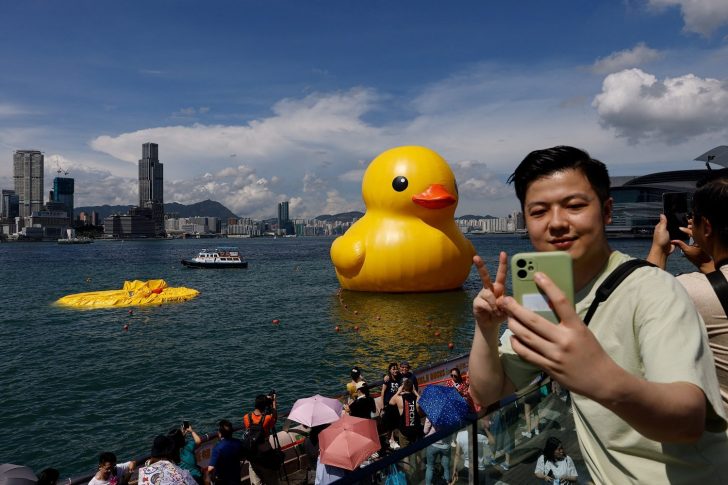 A man poses for a photo with the inflatable yellow ducks created by Dutch artist Florentijn Hofman, one of which is already deflated at Victoria Harbour in Hong Kong