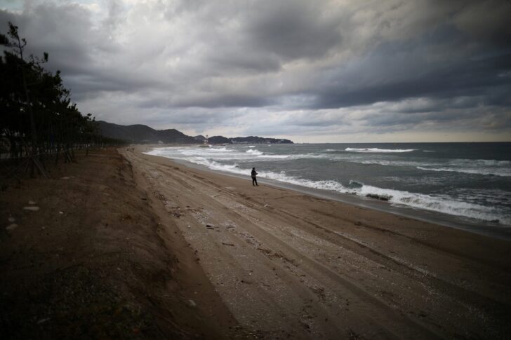 FILE PHOTO: Damage at erosion-affected Maengbang beach is seen as a person fishes in Samcheok