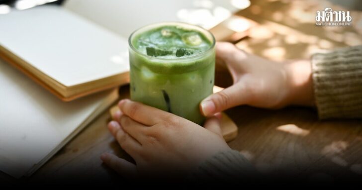 Close-up image of a female holding a glass of iced matcha green tea at a table