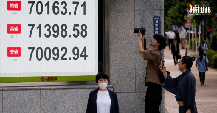 A pedestrian wearing traditional costume takes photo of a stock quotation board showing the Nikkei share average outside a brokerage in Tokyo